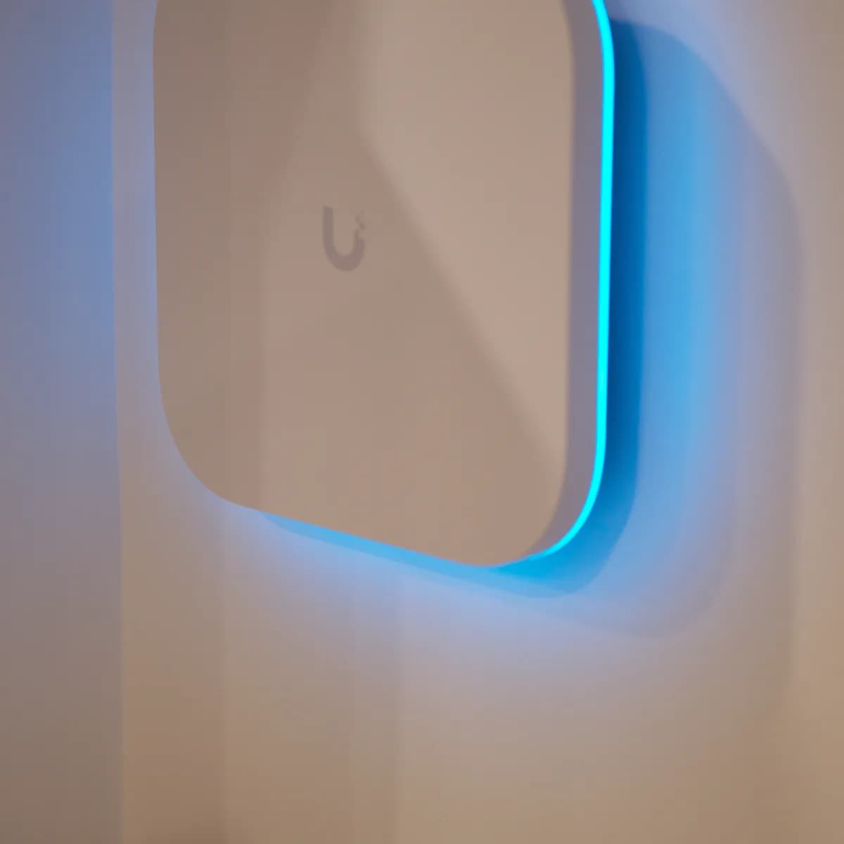 An E7 wall-mounted indoors, its square housing throwing a blue status glow onto the wall behind it.
