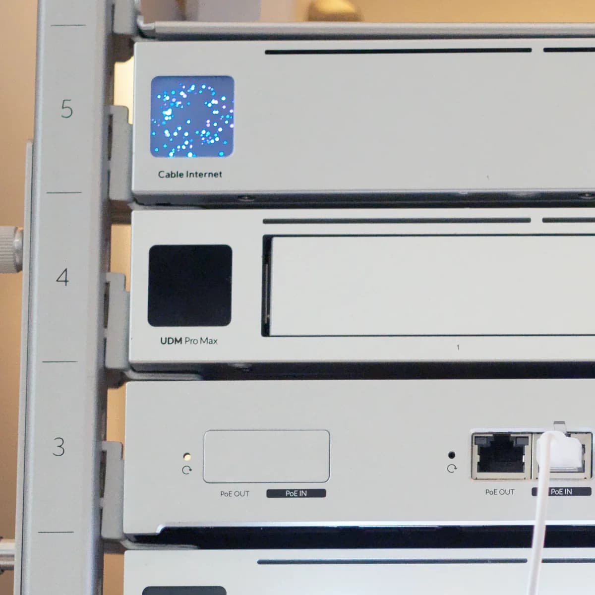 A UDM Pro Max mounted at U4 of a UniFi rack, its front panel labelled, with a patch panel lit below it.
